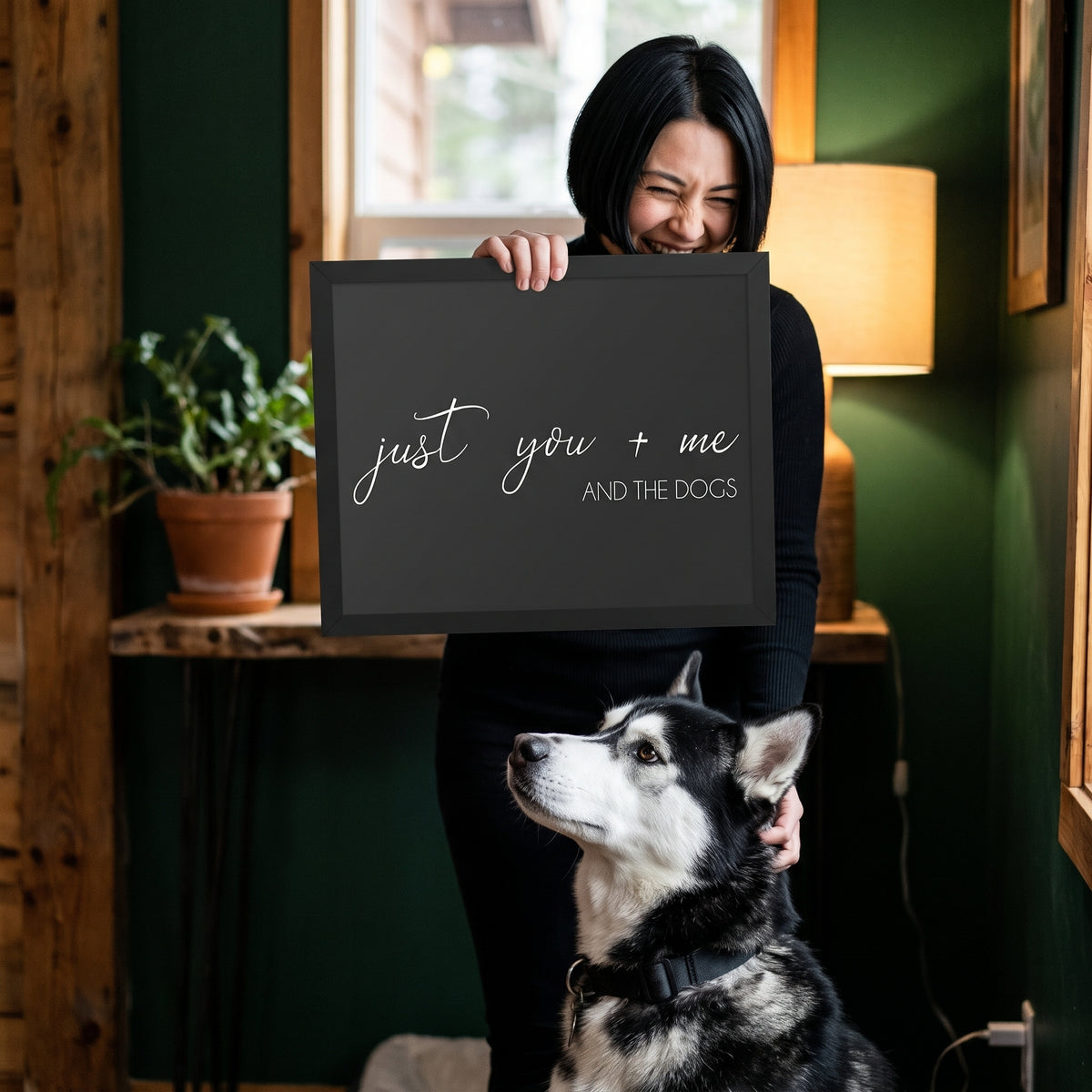 A woman in her 30s with a sleek black bob in a black turtleneck with a quote print (Charcoal / Black Frame) reading You Me and the Dogs, with Koda beside them. [ks Background=Charcoal; Style=Black Frame; kind=lifestyle]
