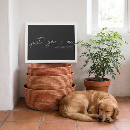 A quote print (Charcoal / White Frame) reading You Me and the Dogs, in a desert-modern home with white plaster walls and terracotta tiles, with Cooper nearby. [ks Background=Charcoal; Style=White Frame; kind=lifestyle]