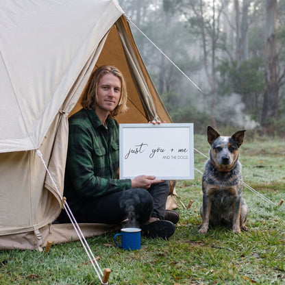 A man in his 30s with shoulder-length blond hair in a forest-green flannel with a quote print (White / White Frame) reading You Me and the Dogs, with Skye beside them. [ks Background=White; Style=White Frame; kind=lifestyle]