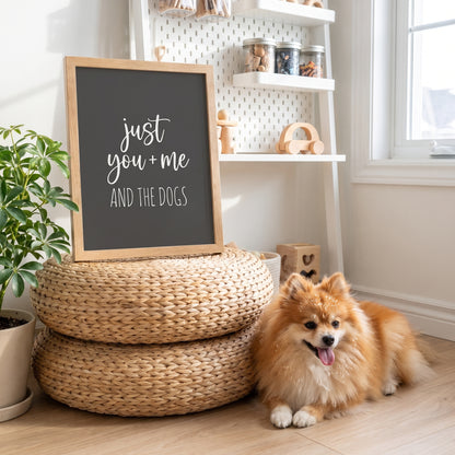A quote print (Charcoal / Oak Frame) reading You Me and the Dogs, in a light-filled nursery-turned-craft room with pegboard shelves, with Nugget nearby. [ks Background=Charcoal; Style=Oak Frame; kind=lifestyle]