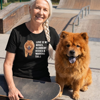A woman in her 70s with a white braid over one shoulder wearing a custom pet t-shirt (Black) printed with "Love Is Wet Noses, Slobbery Kisses & Wagging Tails" and an illustration of Simba the Chow Chow, with Simba beside them. [ks Colour=Black; kind=lifestyle]