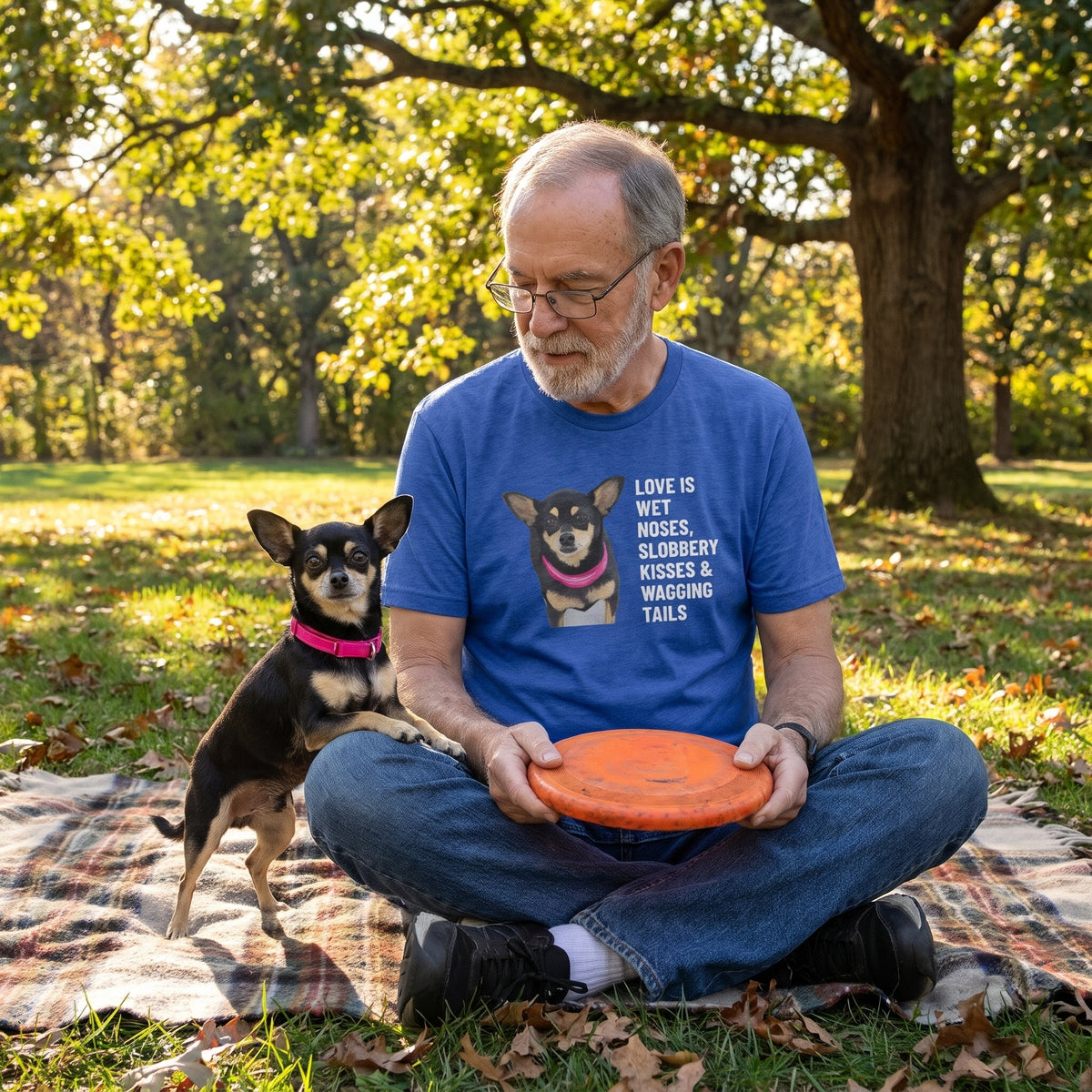 A man in his 70s with a short grey beard, reading glasses wearing a custom pet t-shirt (Heather True Royal) printed with "Love Is Wet Noses, Slobbery Kisses & Wagging Tails" and an illustration of Taco the Chihuahua, with Taco beside them. [ks Colour=Heather True Royal; kind=lifestyle]