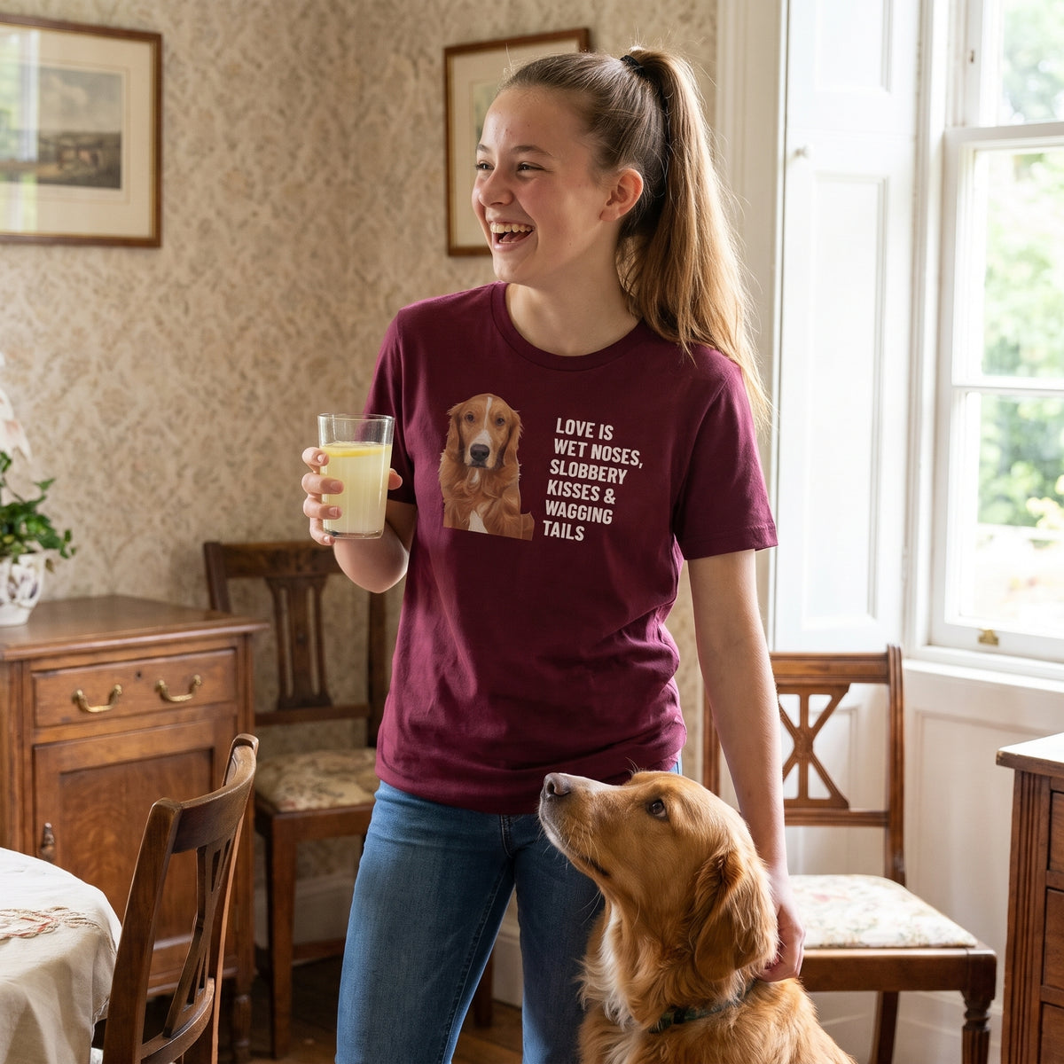 A teenage girl with a high ponytail wearing a custom pet t-shirt (Maroon) printed with "Love Is Wet Noses, Slobbery Kisses & Wagging Tails" and an illustration of Amber the Retriever (Toller type), with Amber beside them. [ks Colour=Maroon; kind=lifestyle]