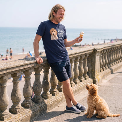 A man in his 30s with shoulder-length blond hair wearing a custom pet t-shirt (Navy) printed with "Love Is Wet Noses, Slobbery Kisses & Wagging Tails" and an illustration of Peaches the Miniature Poodle, with Peaches beside them. [ks Colour=Navy; kind=lifestyle]