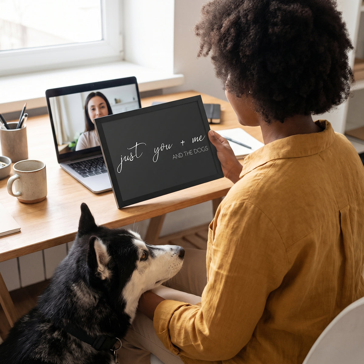 A Black woman in her 30s with natural curly hair in a mustard linen shirt with a quote print (Charcoal / Black Frame) reading You Me and the Dogs, with Koda beside them. [ks Background=Charcoal; Style=Black Frame; kind=lifestyle]